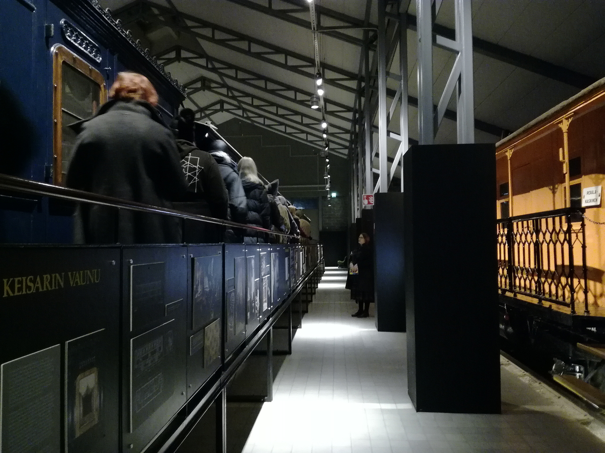 Ryhmä opiskelijoita on kuuntelemassa opasta keisarin junan kävelysillalla Rautatiemuseon näyttelyhallissa.
