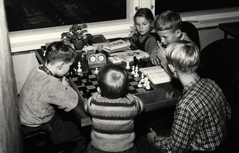 Viisi lasta on pelaamassa shakkia pöydän ääressä.