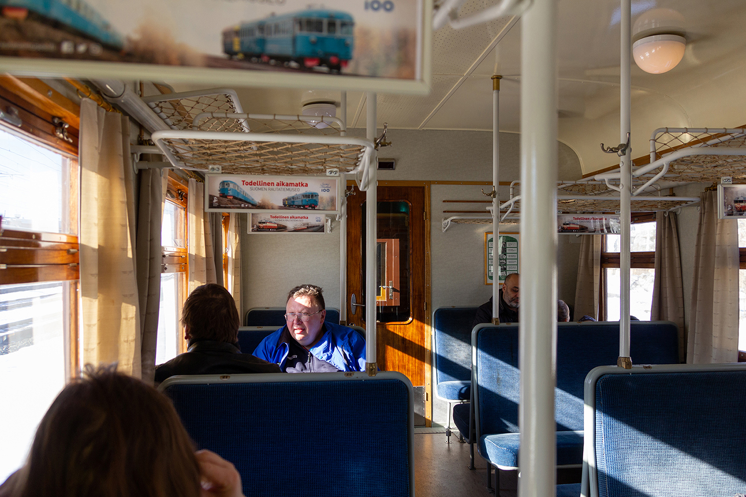 Matkustajia istumassa Perinnejuna Valtterin sinisillä putkisohvapenkeillä.