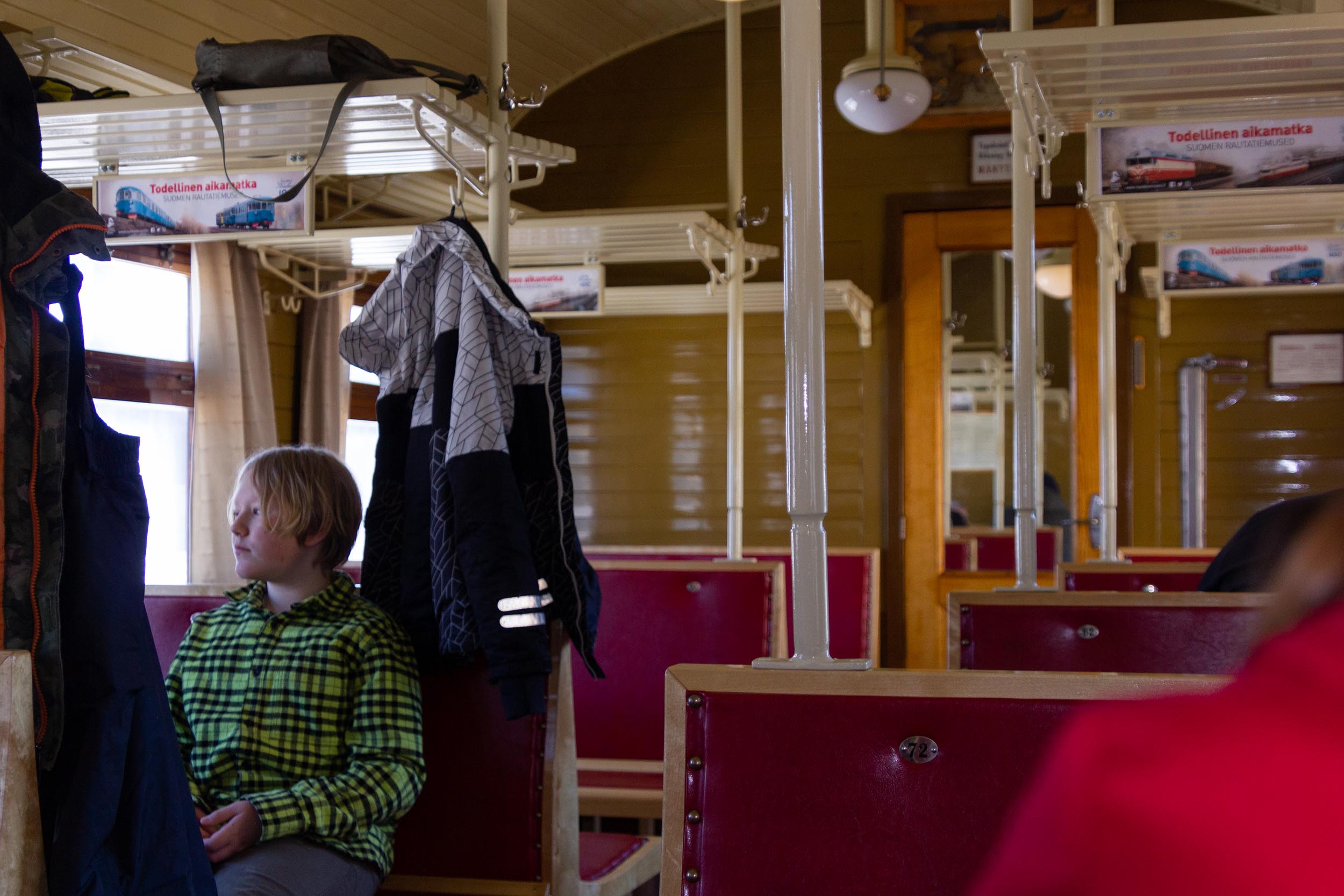 Poika istuu puisella penkillä Perinnejuna Valtterin kolmannen luokan vaunussa ja katsoo ulos ikkunasta.