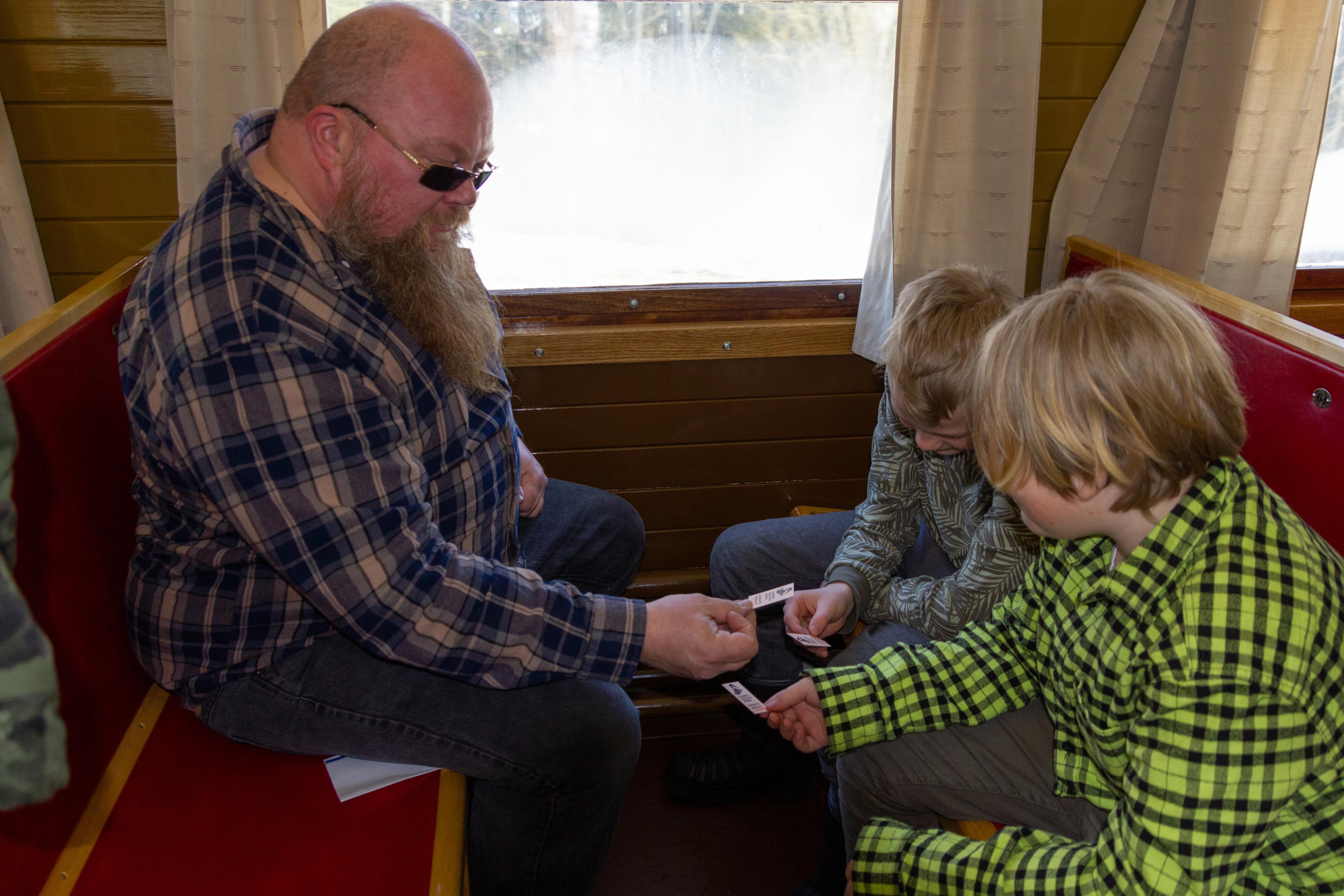 Mies ja kaksi lasta istuvat Perinnejuna Valtterin penkeillä ja tutkivat käsissään olevia pahvisia matkalippuja.