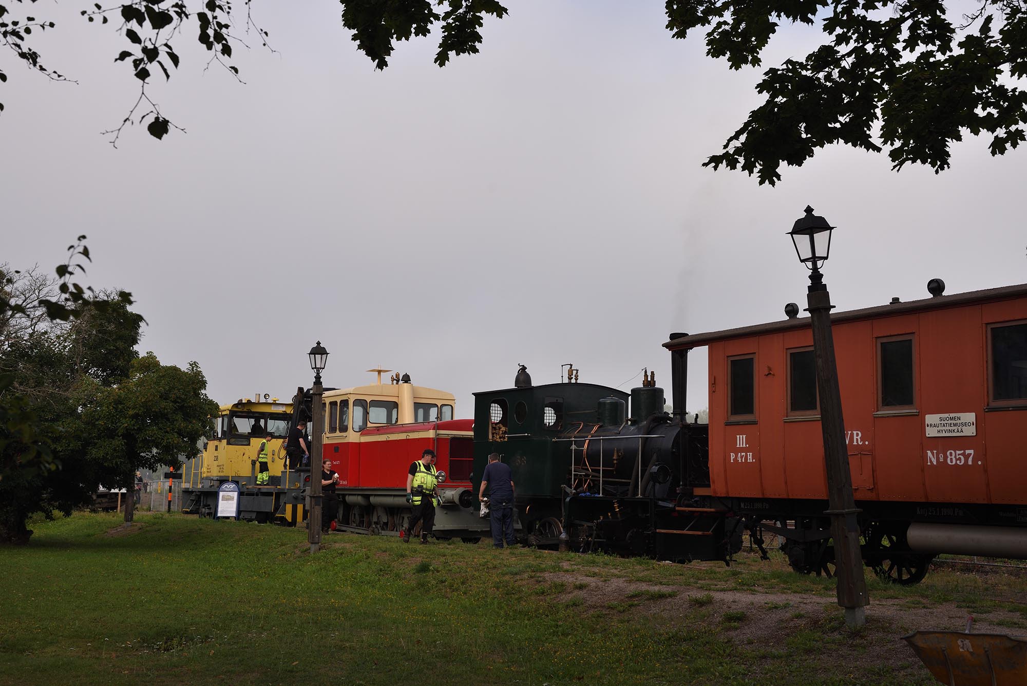 Rautatiemuseon vapaaehtoistyöntekijöitä vetureiden ja vaunujen luona museon raiteella.
